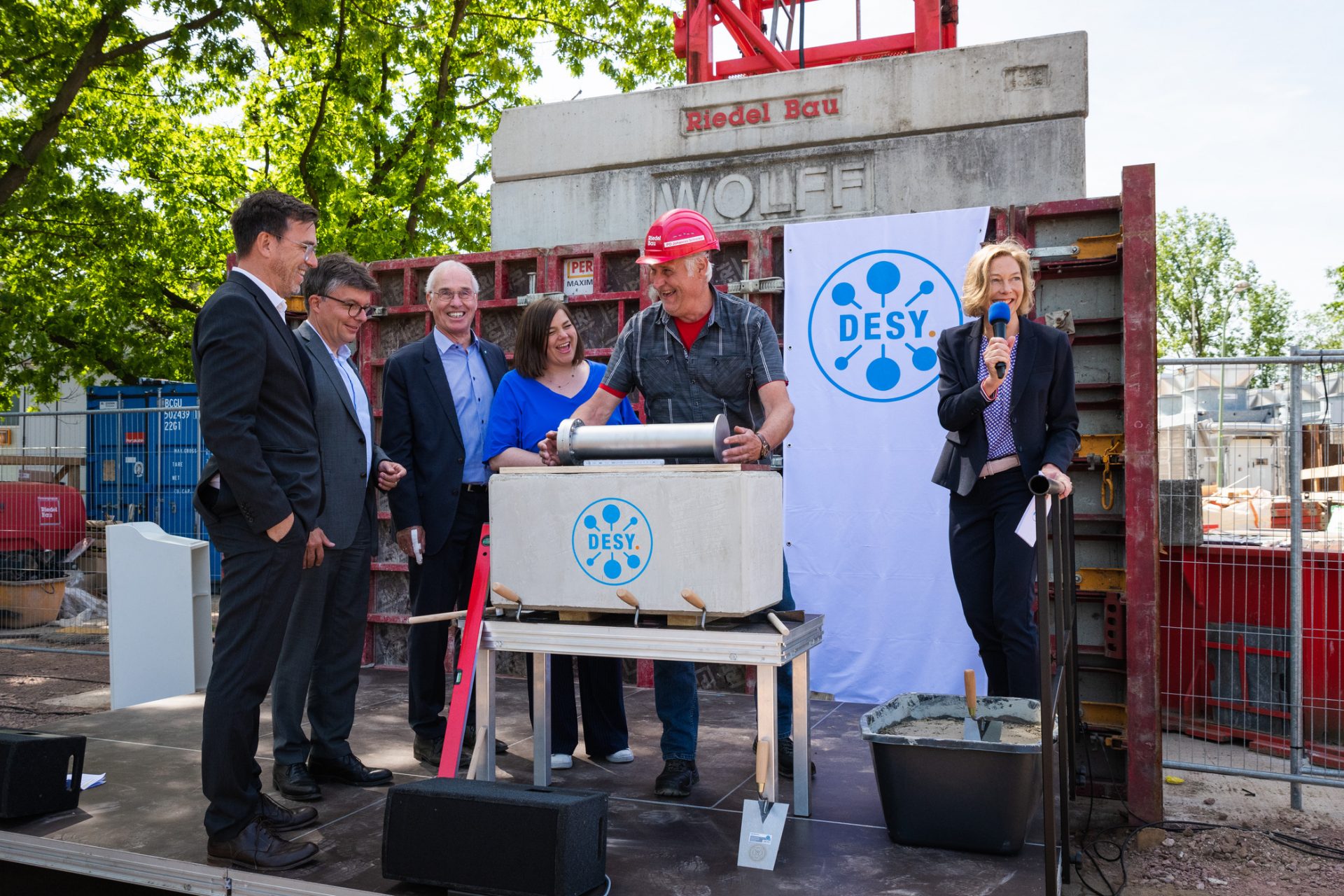 DESYUM foundation stone laying ceremonyForeman Johannes Schrenker (center) of Riedelbau places the time capsule in the foundation stone of DESYUM, under the gaze of architect Matthias Latzke of HPP Architekten, DESY's Administrative Director Christian Harringa, Chairman of the DESY Directorate Prof. Dr. Helmut Dosch, Hamburg's Science Senator and Second Mayor Katharina Fegebank (from left to right) and moderator and DESY Head of Communications Kerstin Straub (far right).